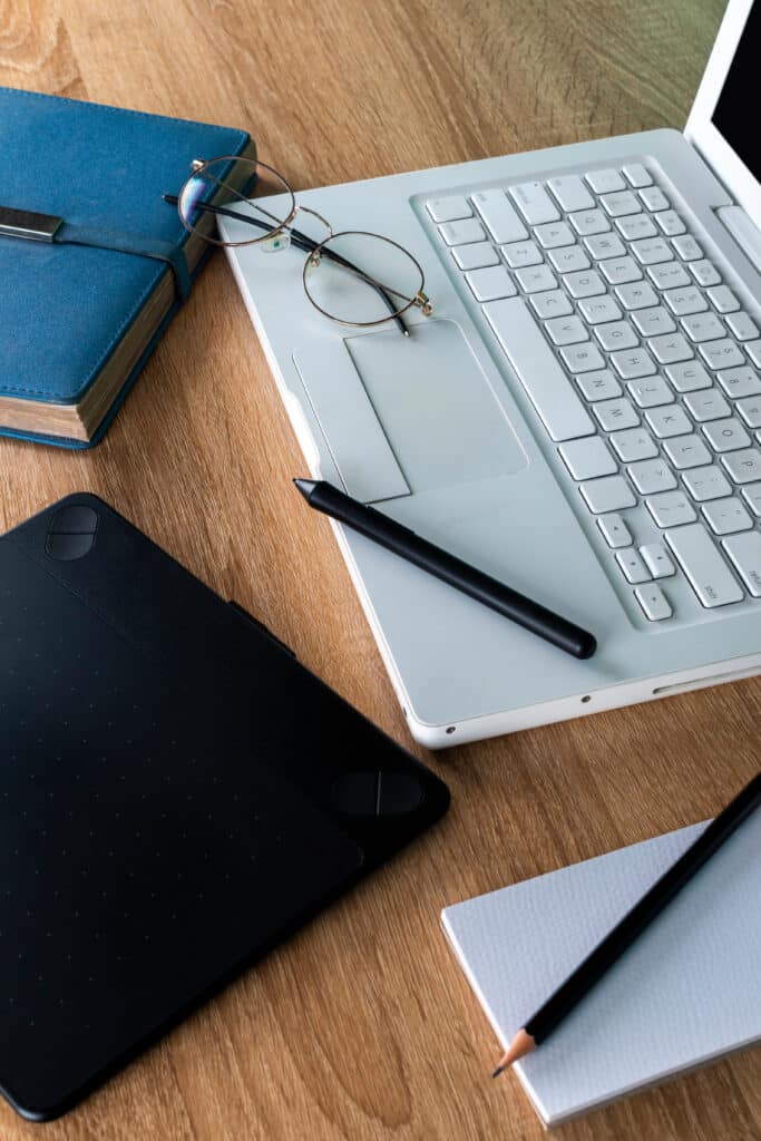 white laptop on a wooden table with blue agenda and graphic tablet, glasses on a white laptop, work and study space, graphic design
