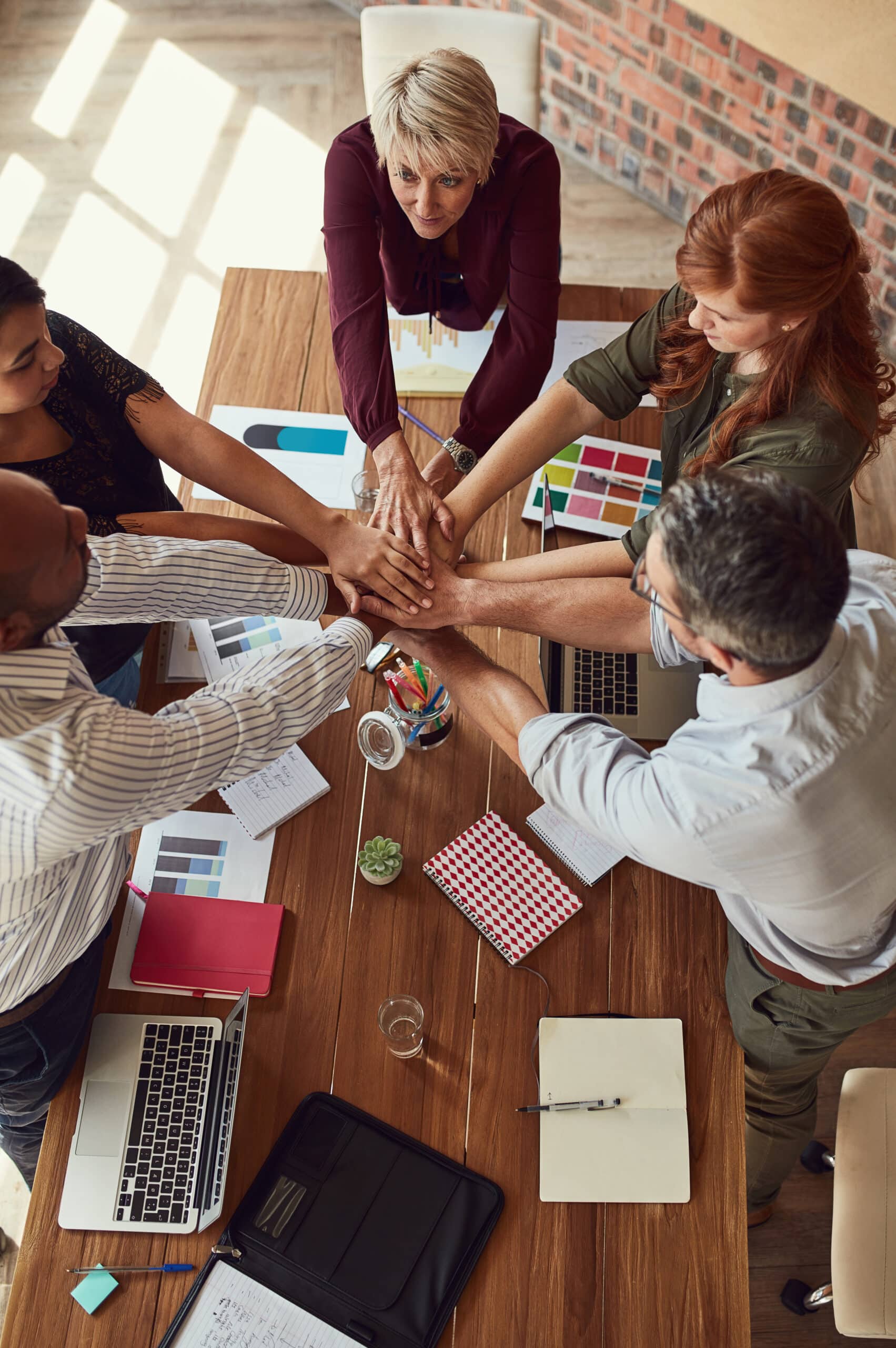 Équipe de professionnels unie, mains jointes au centre d'une table de bureau pour célébrer leur collaboration.