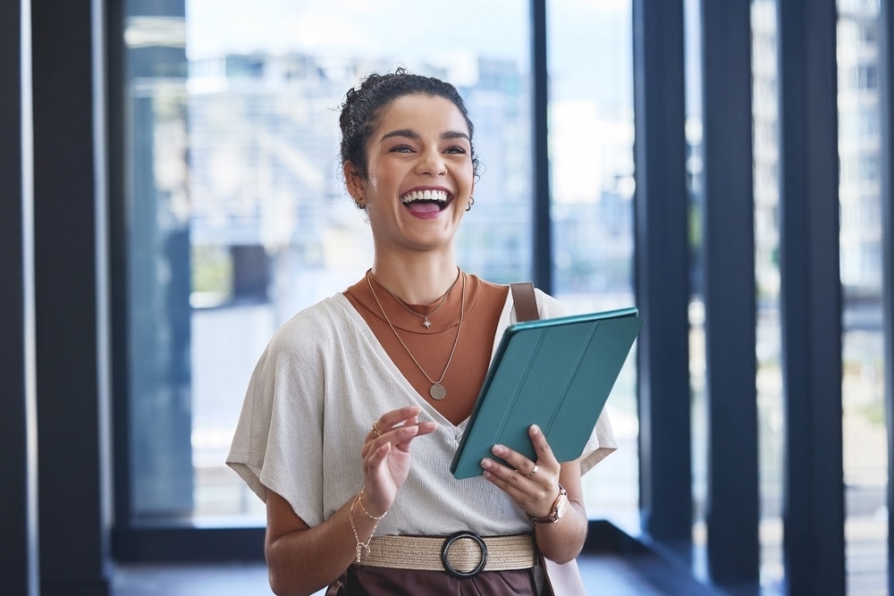 Femme souriante avec une tablette numérique dans un bureau moderne, illustrant la réussite professionnelle.